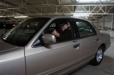 2000 Mercury Grand Marquis - A man holds a gun while sitting in the driver's seat of a tan 2000 Mercury Grand Marquis.