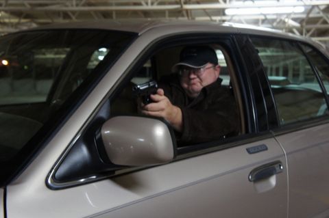 2000 Mercury Grand Marquis - A man aims a handgun from the driver's side window of a tan sedan.