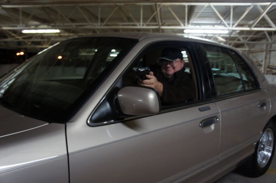Man in a tan 2000 Mercury Grand Marquis holding a handgun