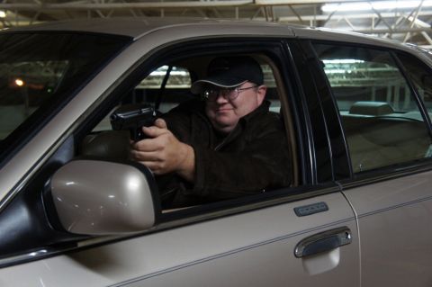 2000 Mercury Grand Marquis - A man sits in the driver's seat of a tan sedan, aiming a handgun out the window.