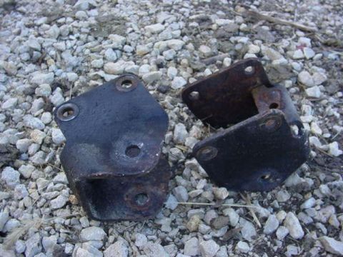 1992 Ford Bronco - Two old, rusted metal brackets lie on a bed of gravel.