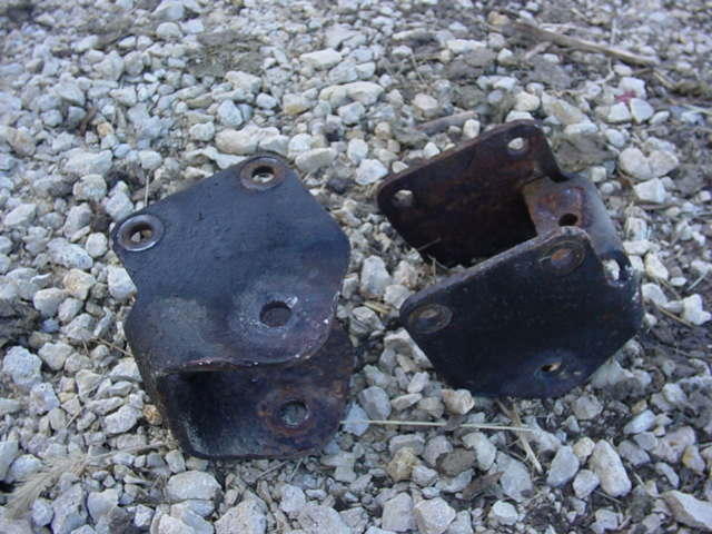 two rusted metal brackets on gravel