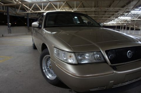 2000 Mercury Grand Marquis - Gold 2000 Mercury Grand Marquis with aftermarket wheels parked in a garage.