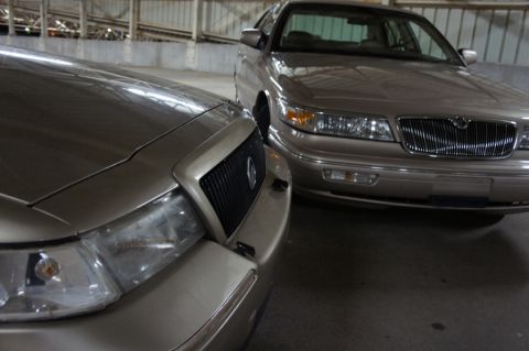 2000 Mercury Grand Marquis - Two tan sedans are parked indoors, with the front of one vehicle partially obscuring the other.