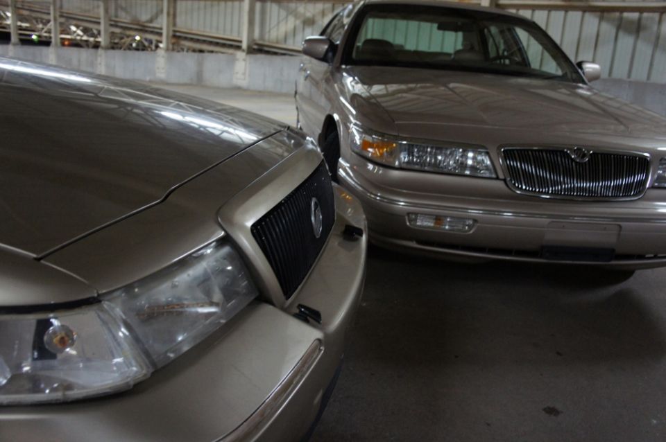Two tan sedans parked, one in foreground angled left, the other behind it