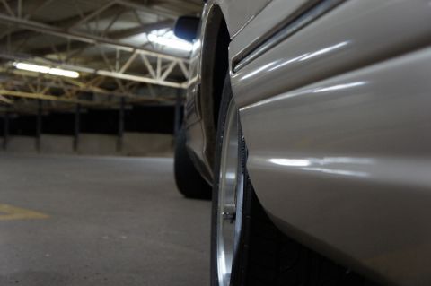 2000 Mercury Grand Marquis - A low-angle shot captures the side profile of a tan sedan, focusing on the wheel and the car's body panel.