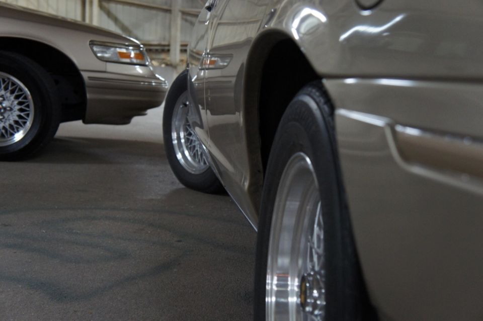 Close-up of the side of a tan sedan, with another tan sedan visible behind it. Both have wire-spoke wheels