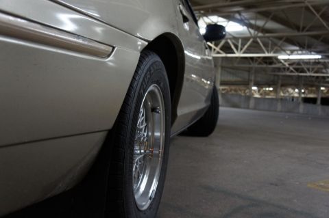 2000 Mercury Grand Marquis - A close-up side view of a tan sedan, highlighting its chrome trim and wire wheels, parked indoors.
