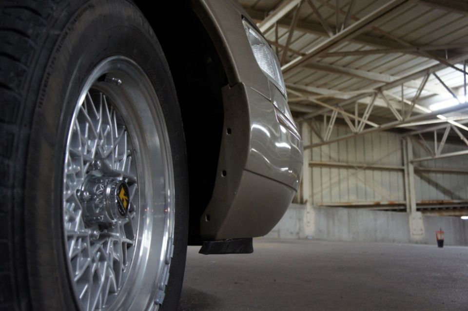 Close-up of a car's front fender and wire-spoke wheel in an indoor space