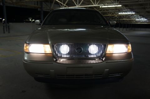 2000 Mercury Grand Marquis - A gold Mercury Grand Marquis is parked in a garage at night, its headlights illuminated.