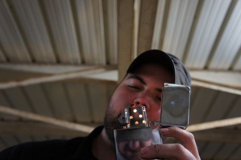 2000 Mercury Grand Marquis - A man lights a Zippo lighter under a corrugated metal roof.