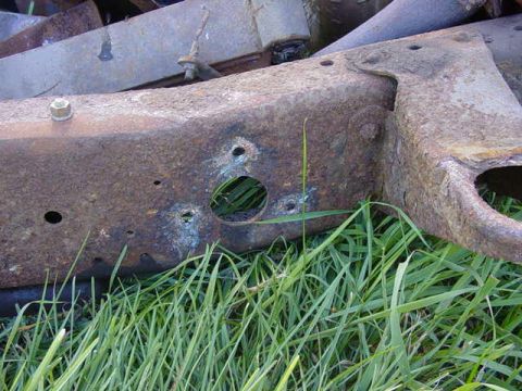 1992 Ford Bronco - A close-up view of a heavily rusted vehicle frame section, partially obscured by grass. The registry information may be inaccurate.