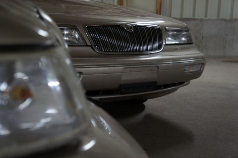 2000 Mercury Grand Marquis - The front grille and headlights of a Mercury Grand Marquis are visible, partially obscured by another vehicle.