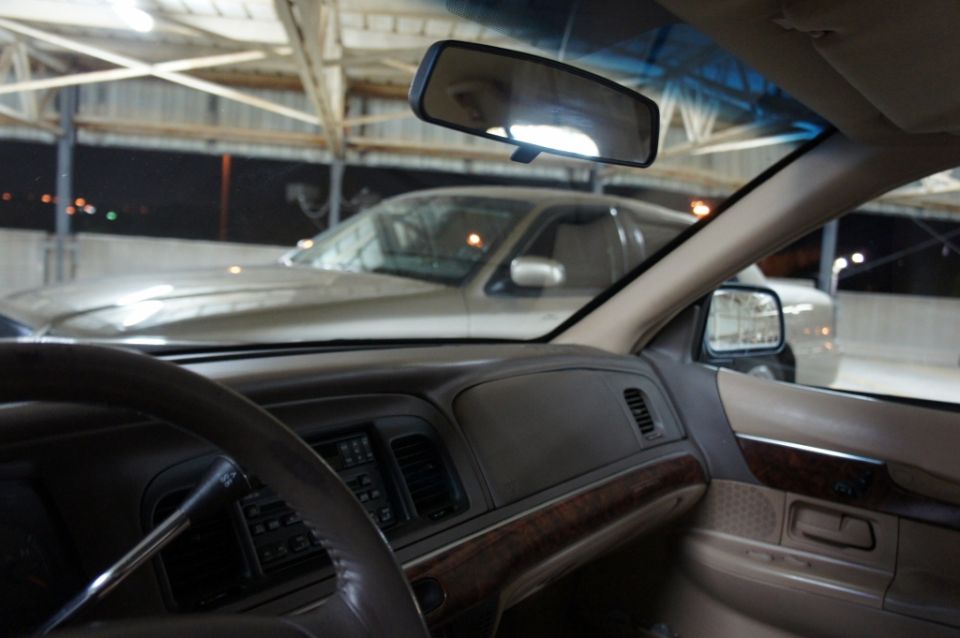 Interior view of a 2000 Mercury Grand Marquis, showing dashboard and steering wheel. Another car is visible outside
