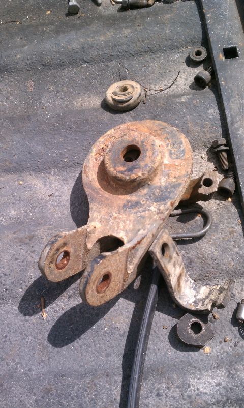 1990 Ford Bronco - A rusted metal bracket, likely a suspension component, lies on a textured surface with surrounding hardware.