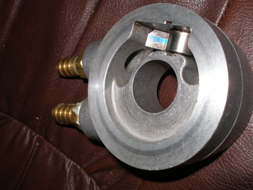 Aluminum oil filter adapter with two brass fittings on a brown textured surface