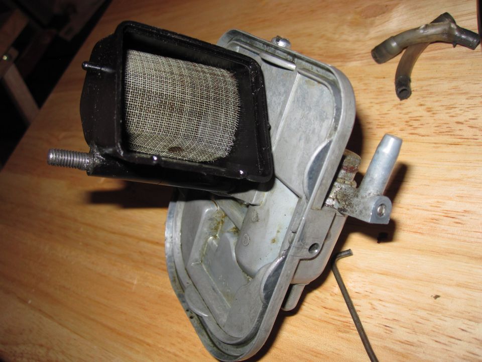 Motorcycle carburetor with mesh air filter screen, metal housing, and attached hoses on a wooden surface