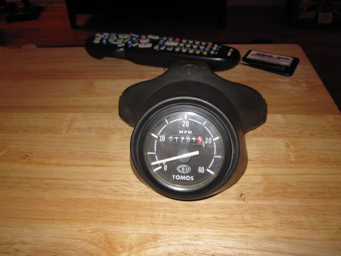 1981 Garelli Rally Sport - A Tomos branded speedometer is shown on a wooden surface, with a remote control and cassette tape in the background.