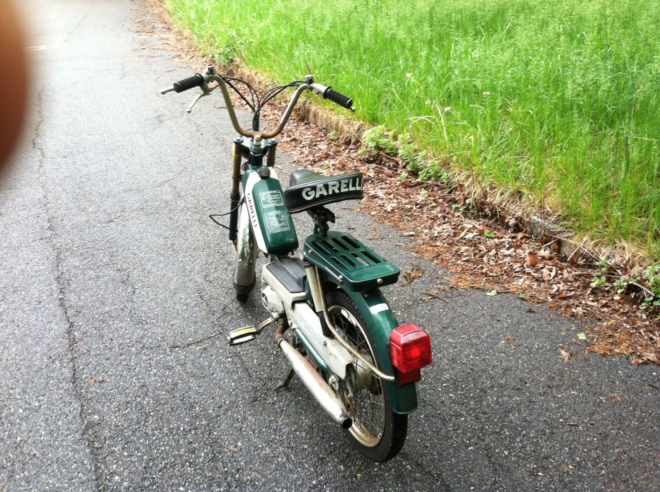 Green moped parked on a paved path with grass on the side. Has a Garelli logo on the seat