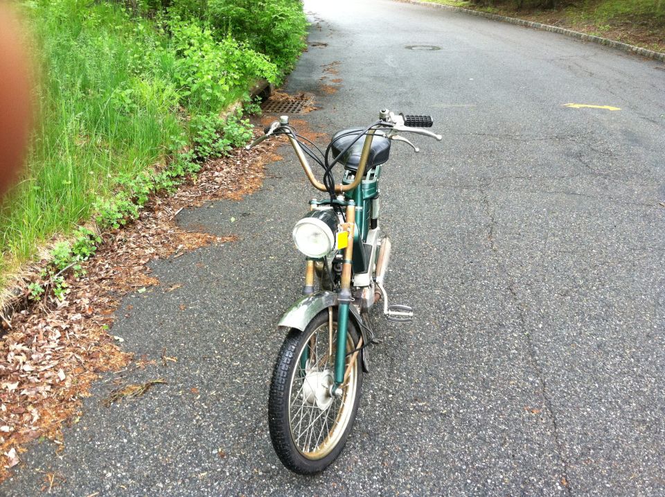 Green moped with chrome accents parked on an asphalt road