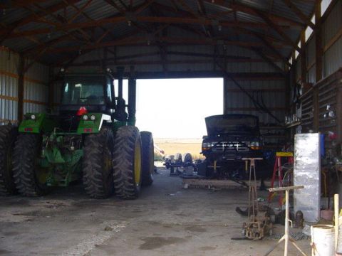 1992 Ford Bronco - A large green tractor and a dark-colored truck are parked inside a barn, with various tools and equipment visible.