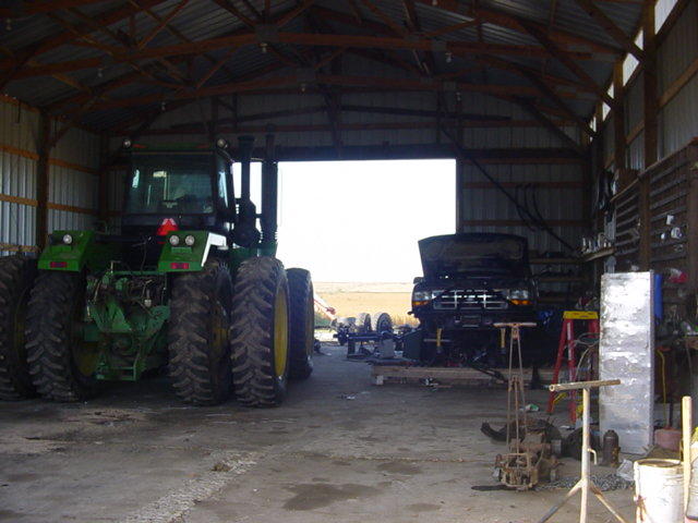 Tractor and a truck with hood up inside a barn. Tools and equipment are scattered around