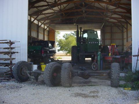 1992 Ford Bronco - A barn houses a tractor chassis and a green tractor, with a black truck visible in the background.