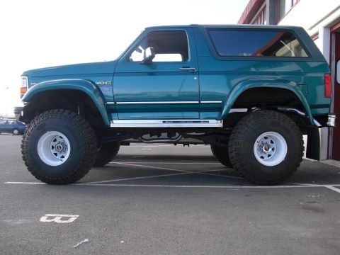 1996 Ford Bronco - Side profile of a lifted 1996 Ford Bronco SUV parked on asphalt.