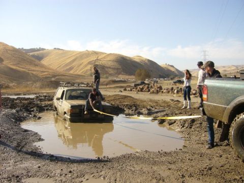 1990 Ford Bronco - A 1990 Ford Bronco is stuck in a mud pit while people attempt to help.