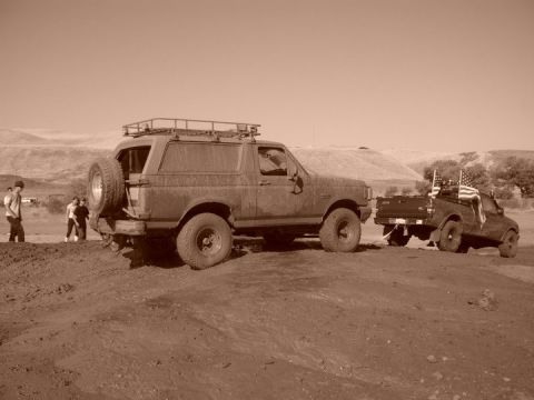 1990 Ford Bronco - Two trucks are stuck in the mud, one a Bronco and the other a pickup truck with flags.