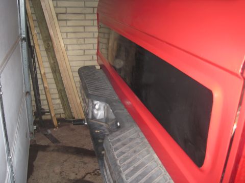 1979 Ford Bronco - The rear section of a red pickup truck is visible, parked indoors next to lumber.