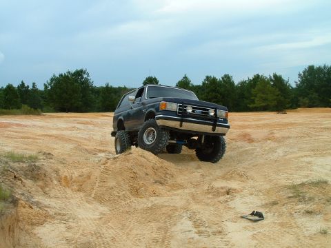 1995 Ford Bronco - Ford Bronco navigates a challenging sandy terrain with trees in the background.