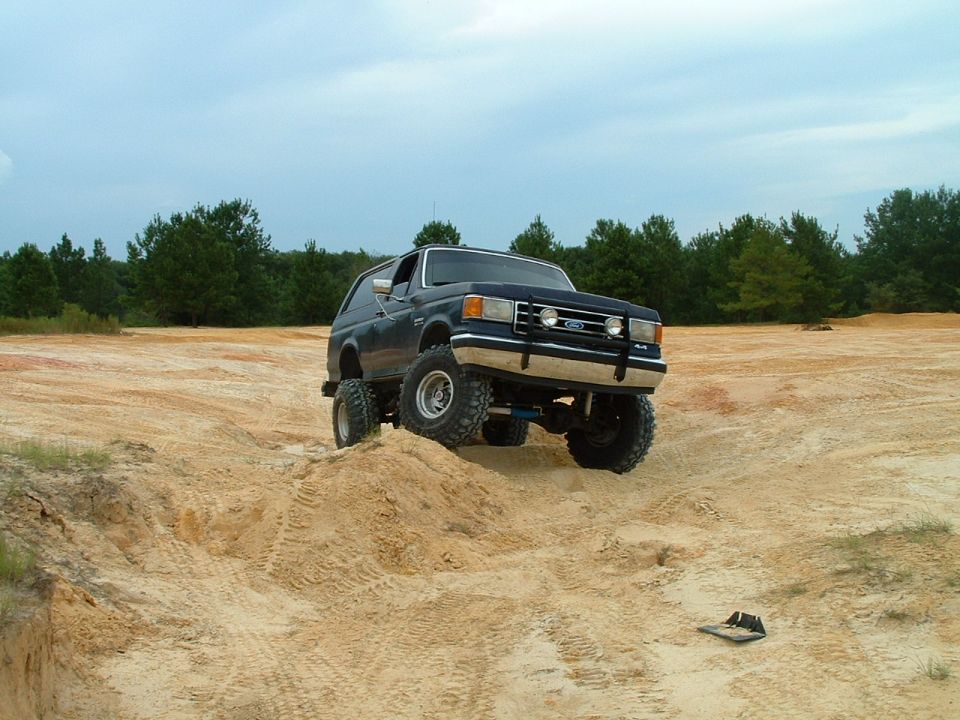 Dark blue Ford Bronco with lifted suspension driving on a sandy hill