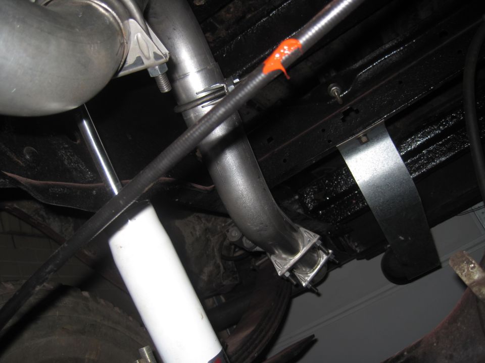Close-up of exhaust pipe, U-bolts, and a white shock absorber under a vehicle