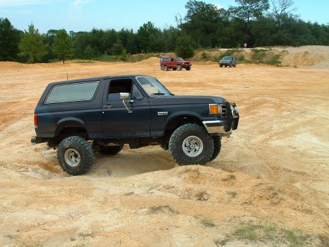 1995 Ford Bronco - A lifted Ford Bronco navigates a sandy, off-road course with other SUVs visible in the distance.