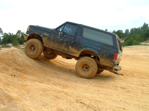 1995 Ford Bronco - Mud-covered 1995 Ford Bronco tackles a steep dirt incline off-road.