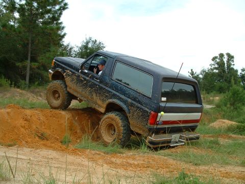 1995 Ford Bronco - A 1995 Ford Bronco navigates a challenging off-road course, kicking up dirt.