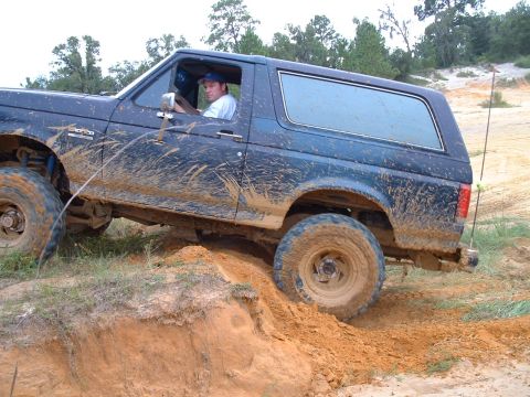 1995 Ford Bronco - 1995 Ford Bronco navigating a muddy off-road trail with a driver inside.