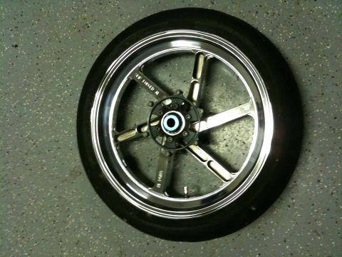 1996 Ford Bronco - A single motorcycle wheel with a polished five-spoke design and tire is shown on a textured surface.