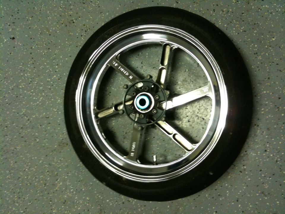 Motorcycle wheel with five spokes and a chrome rim, resting on a speckled gray floor