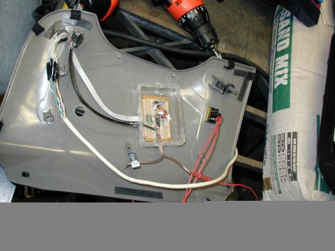 2000 Ford Taurus - The back side of a gray interior trim panel laid on a workbench with a custom circuit on perfboard mounted in a clear plastic project box,…