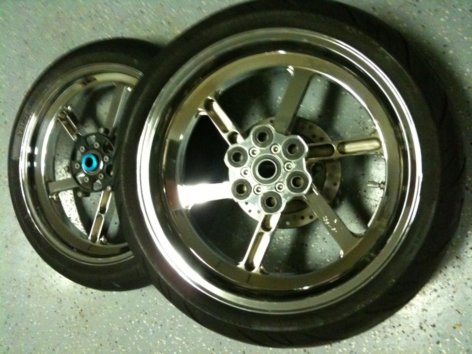 Two chrome motorcycle wheels with tires and brake rotors on a speckled floor
