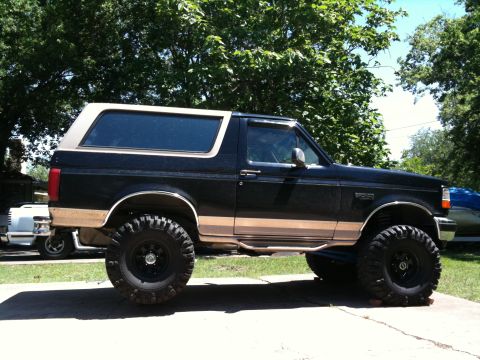 1996 Ford Bronco - This lifted Ford Bronco sits parked on a concrete driveway, its off-road tires and two-tone paint scheme.