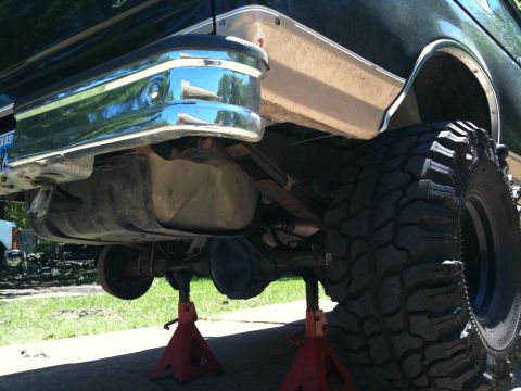 1996 Ford Bronco - The rear of a 1996 Ford Bronco is shown lifted on red jack stands with a chrome bumper and large off-road tire visible.
