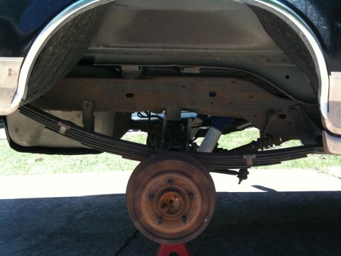 1996 Ford Bronco - Undercarriage view showing the rear suspension and brake drum assembly of a vehicle, supported by a jack stand.