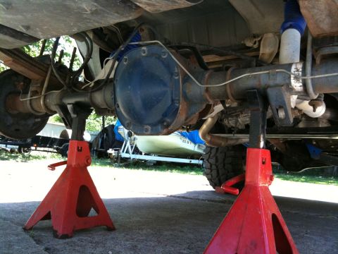 1996 Ford Bronco - The rear axle assembly of a vehicle is supported by red jack stands, with suspension and exhaust components visible.