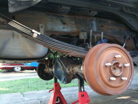1996 Ford Bronco - The underside of a vehicle shows its rear axle, leaf springs, and brake drum, with another vehicle partially visible in the background.