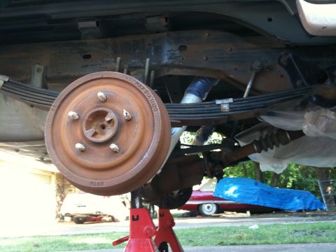1996 Ford Bronco - The rear suspension and brake drum of a vehicle are visible while it is supported by jack stands.