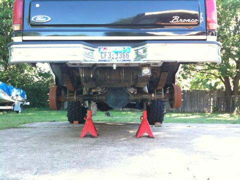 1996 Ford Bronco - The rear underside of a dark blue Ford Bronco is visible, supported by red jack stands, with its wheels removed.