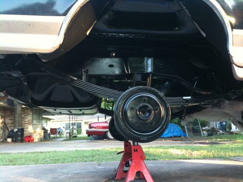 1996 Ford Bronco - The undercarriage of a vehicle is shown, supported by red jack stands, with a focus on the rear suspension components.